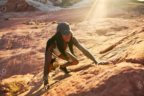 Preview: High angle view of female african american hiker climbing rock at Valley of Fire in nevada desert