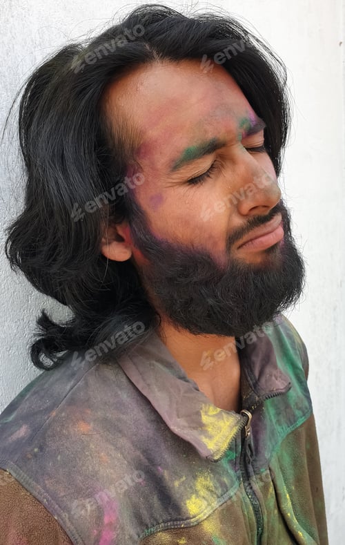 Preview: Side view of handsome young man covered with multi color holi powder with white wall background