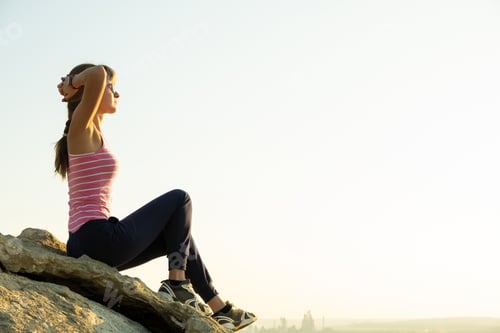 Preview: Woman hiker sitting on a steep big rock enjoying warm summer day. Young female climber resting