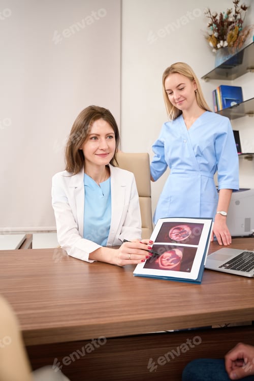 Preview: Gynecologist showing to couple results of ultrasound scanning of woman belly