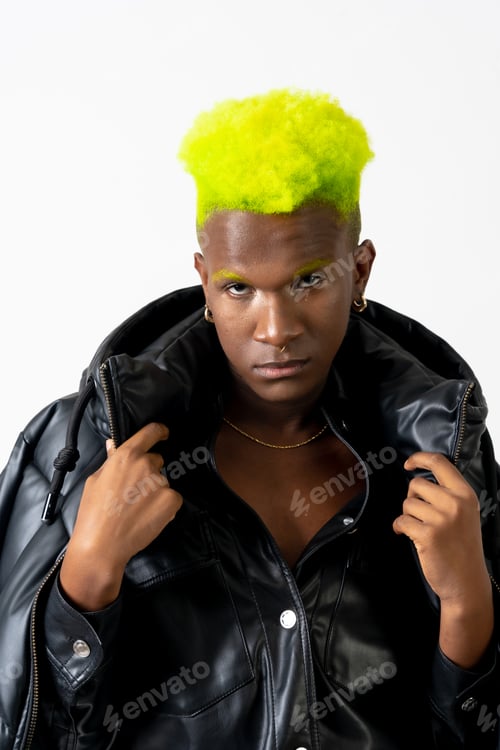 Preview: Black ethnic man in studio with white background, LGTBI concept, looking at camera with black jacket