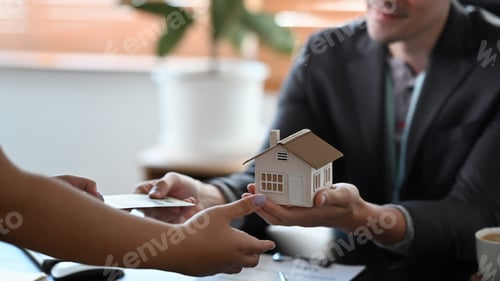 Preview: Cropped image of male estate agent holding house model and give proposal to customer.