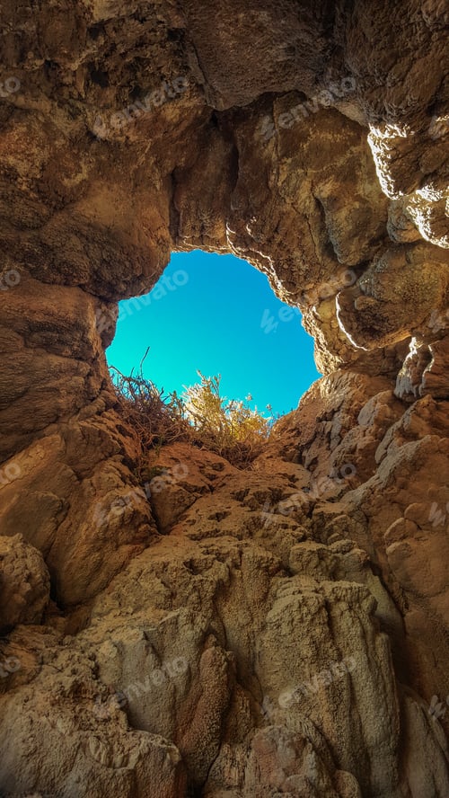 Preview: A small hole in a rock wall with a blue sky above