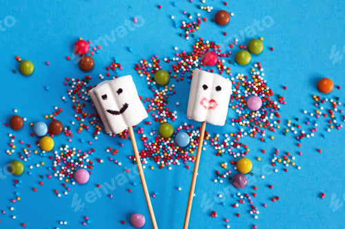 Preview: marshmallows on wooden skewers with color sweets on blue background.