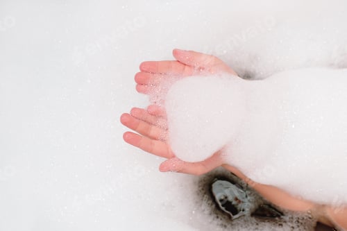 Preview: baby's hands holding bath foam. girl having fun in the bathroom. child bathing. crop view.