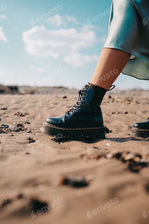 Preview: Woman’s leg in brutal trendy boots walking in dessert. Young lady in silk skirt and rough shoes