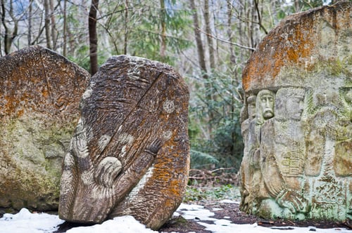 Preview: Ancient large stones with engraving at green forest with little snow cover in Carpathians mountains.
