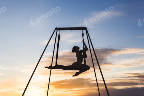Preview: Beautiful girl practicing fly-yoga poses in a hammock outdoor at sunset