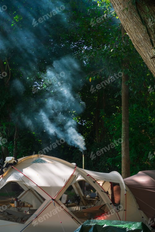 Preview: Morning sunlight on surface of tents with smoke from cooking pipeline under big tree in the forest