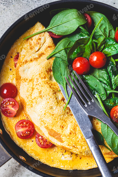 Preview: Omelet with fresh spinach and tomato salad in frying pan on gray table. Breakfast food.