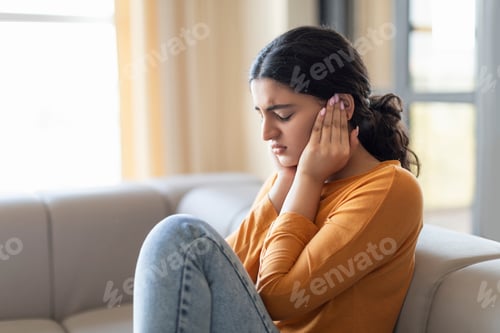 Preview: Upset young woman sitting on couch and covering her ears with hands