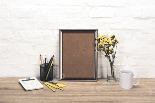 Preview: close up view of empty photo frame, office supplies, coffee cup and flowers in vase on table