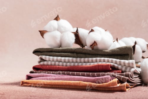 Preview: Stack of colored serving napkins and branch of cotton on beige background