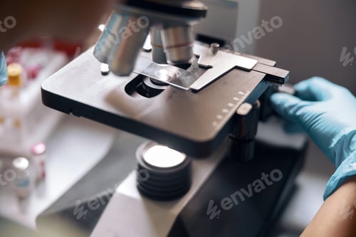 Preview: Woman lab assistant adjusts microscope with sample on slide in laboratory closeup