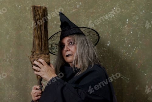 Preview: Closeup of a white-haired witch in a black hat and costume holding a broom