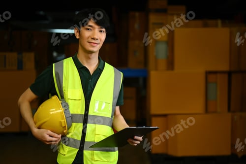 Preview: Portrait of handsome male worker holding hard hat standing at retail warehouse.