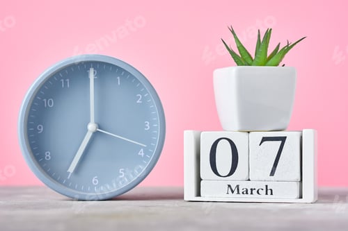 Preview: Wooden block calendar with date 7 march, alarm clock and plant on the pink background
