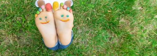 Preview: Children's feet with a pattern of paints smile on the green grass. Selective focus.