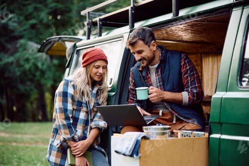 Preview: Happy couple using laptop while relaxing in camper trailer in the woods.