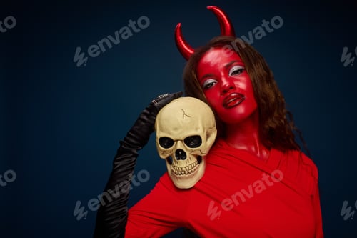 Preview: A captivating woman dressed as a devil holds a skull, embodying Halloween spirit and allure