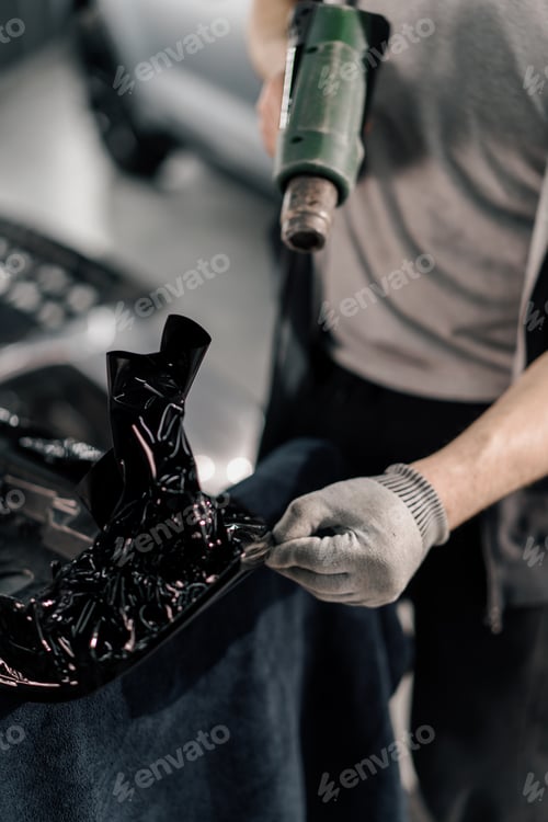 Preview: A worker covers a car spoiler with a film in the workshop using a hair dryer and a spatula