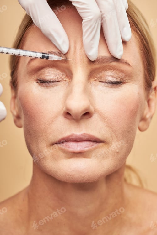 Preview: Close up of beautician hands in protective gloves making injection in female forehead