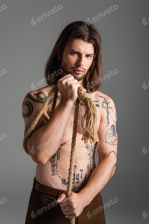 Preview: Shirtless tattooed man holding rope and looking at camera isolated on grey