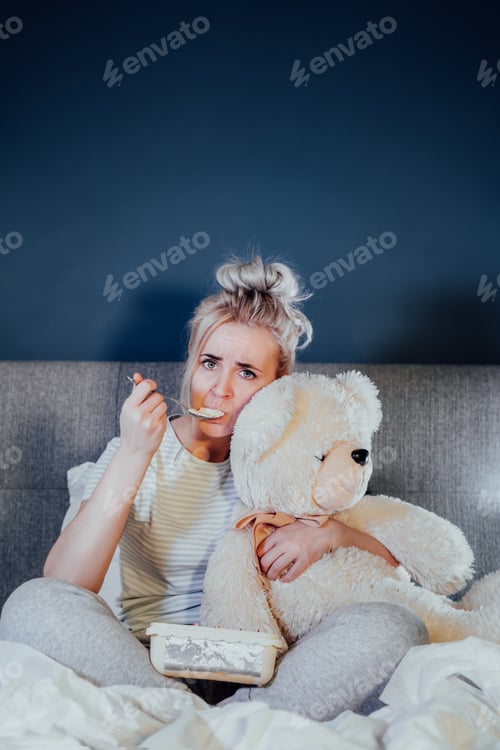 Preview: Heartbroken young woman huggying big teddy bear, eating ice cream from bucket while watching movie
