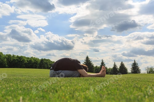 Preview: Young man stretching on green grass before yoga or fitness in park