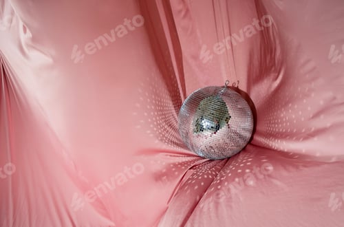 Preview: Shimmering disco ball resting on soft pink fabric, reflecting light patterns