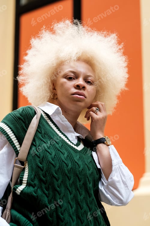 Preview: Portrait of proud albino woman looking down at camera with colorful background.
