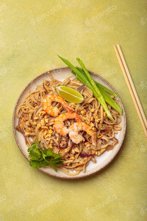 Preview: Bowl of pad thai noodles garnished with shrimps and lime on green background, traditional dish of