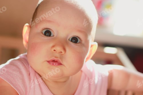 Preview: Cute little toddler girl standing in her small bed and seriously looking at camera