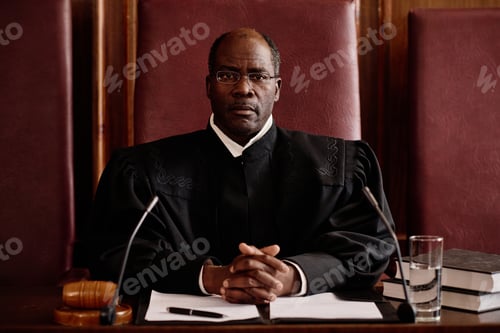 Preview: Confident experienced male judge in eyeglasses and black mantle sitting by desk