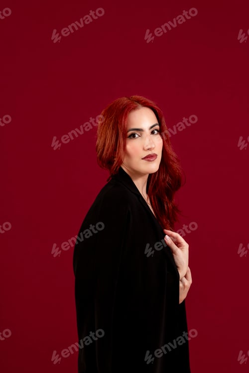 Preview: Confident woman looking at the camera while posing against a red isolated background.