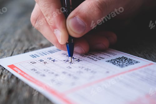 Preview: A man is hand crosses out the numbers in a lottery ticket with a pen on a wooden table.