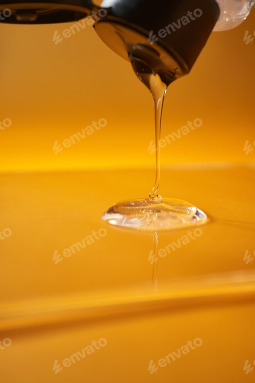 Preview: A drop of body gel or shampoo pouring from above on a yellow saturated background.