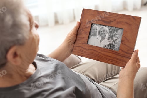 Preview: Elderly woman with framed family portrait at home