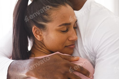 Preview: Happy diverse couple embracing by window at home, woman smiling