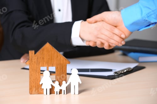 Preview: Man shaking hands with real estate agent at table, focus on family and house figures. Home insurance