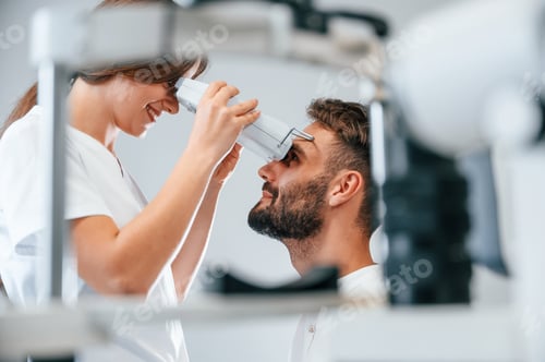 Preview: Side view. Man's vision checked by female doctor in the clinic by using special optometrist device