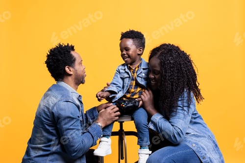 Preview: Joyful little child playing around with a joystick and sitting next to his parents
