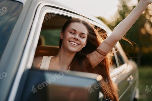 Preview: Happy young woman with long hair enjoying a road trip, smiling while leaning out of a car window