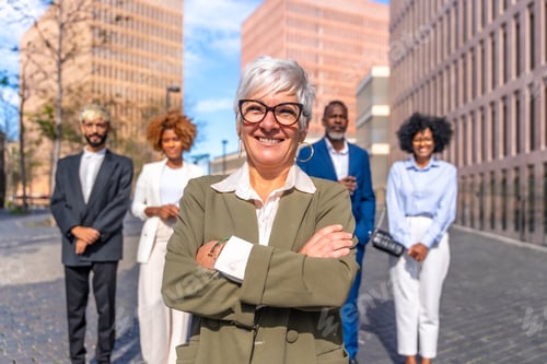 Preview: Mature smiling businesswoman standing proud next to colleagues