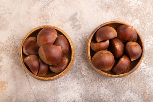 Preview: wooden bowl with raw edible Сhestnuts on brown concrete, top view, flat lay, close up, minimalism
