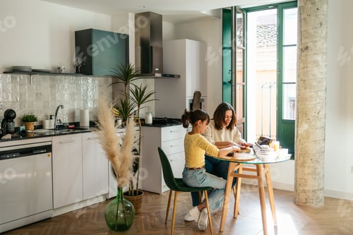 Preview: Mom and daughter making chocolate cookies following online recipe on tablet in bright kitchen
