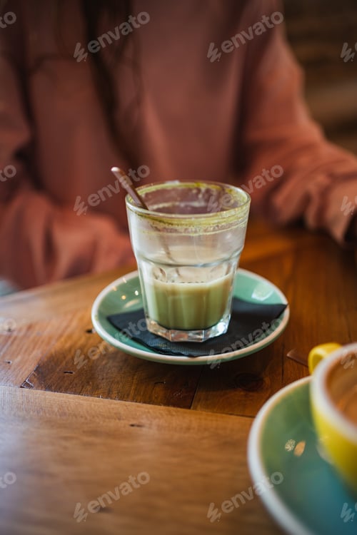 Preview: Close up view of half drunk matcha tea glass on wooden table at restaurant
