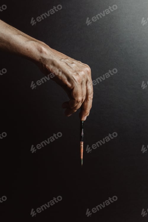 Preview: Hands of old female artist holding messy dirty paint brushes with different paints