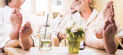 Preview: close up of feet of couple of seniors on the tale in a resort hotel or at home with a cocktail
