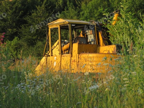 Preview: Old yellow excavator on a field near a forest